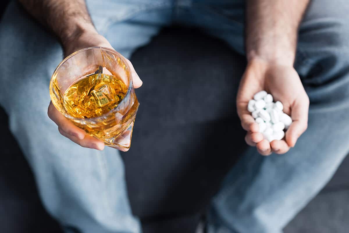 Man holding a glass of alcohol and xanax in the other hand