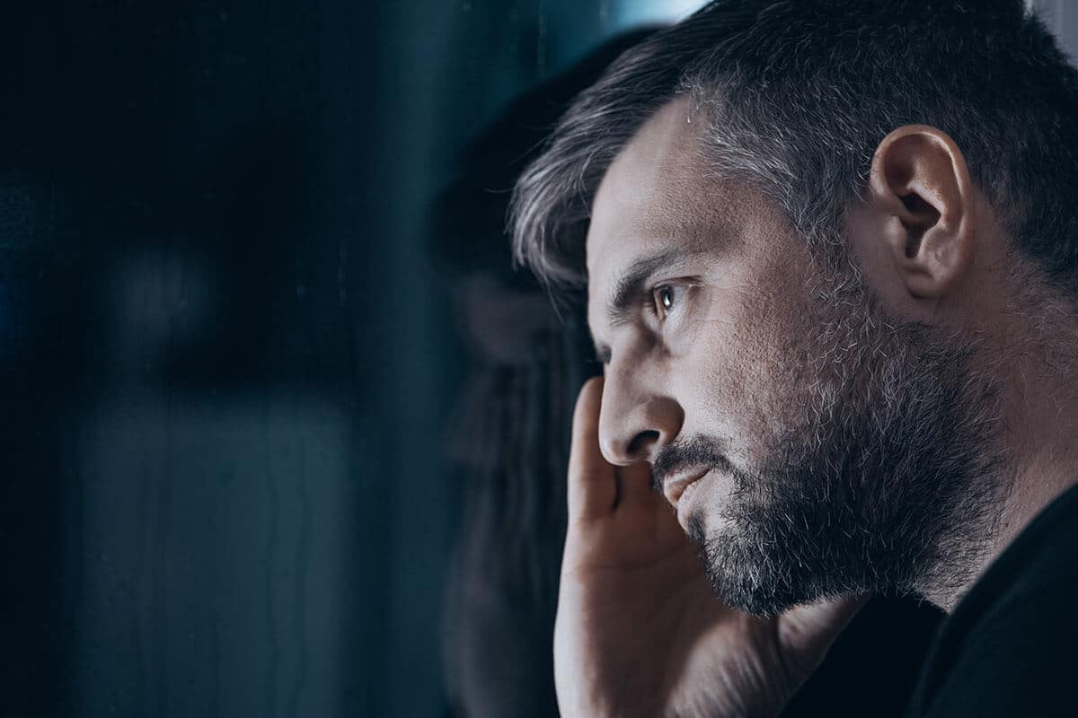 Man in dark with hand to head struggling through alcohol withdrawal symptoms