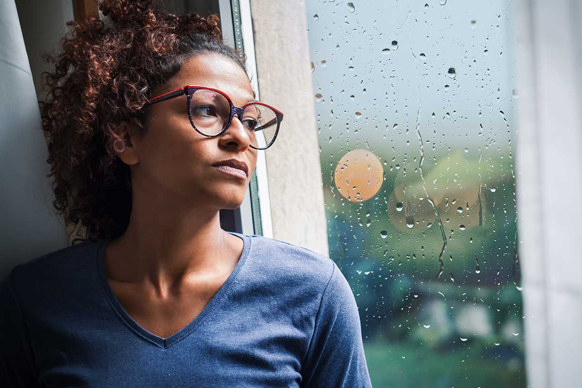 A woman stares out the window on a rainy day, wondering about the alcohol withdrawal timeline